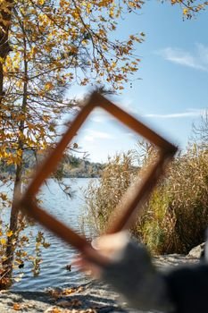 Creative view of a tranquil autumn lake with trees and reeds through a handheld frame.