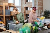 Two women sorting glass and plastic waste in an indoor recycling center.
